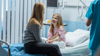 Young girl sitting in hospital bed talking to her mum