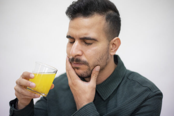 Young adult drinking cold juice and displaying teeth sensitivity - needs dental health check