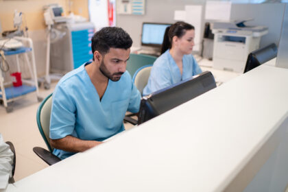 Hospital front desk staff dressed in blue scrubs, working diligently on computers, showcasing the administrative side of healthcare.