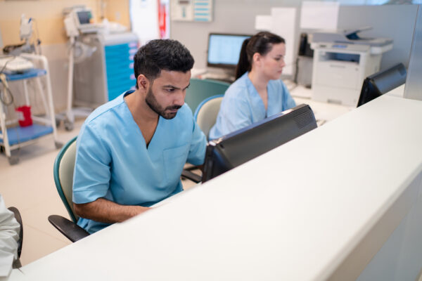 Hospital front desk staff dressed in blue scrubs, working diligently on computers, showcasing the administrative side of healthcare.