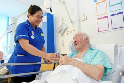 Nurse in a hospital ward offering a glass of water to an elderly patient in bed.