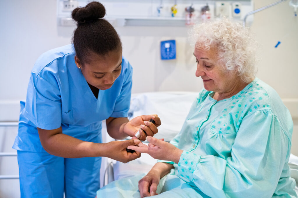 Young nurse doing blood sugar test of senior patient sitting in hospital