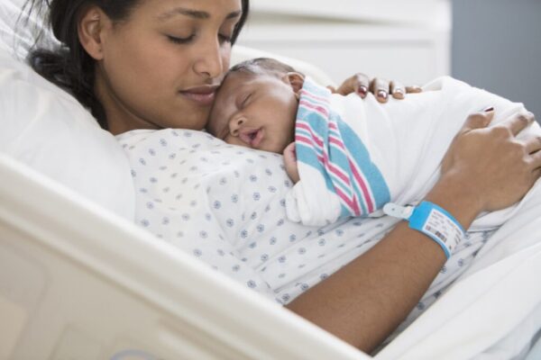 Woman of colour holding a newborn baby while sitting in a hospital bed