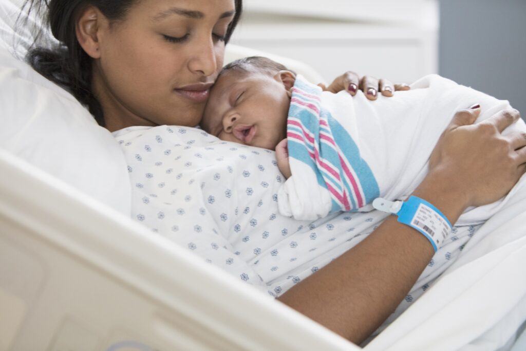 Woman of colour holding a newborn baby while sitting in a hospital bed