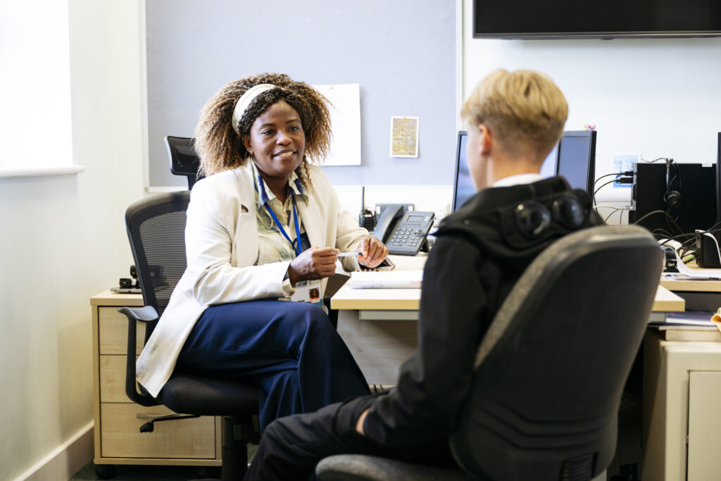 Femal GP smiling at patient in office, next to IT set up