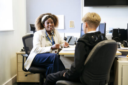 Femal GP smiling at patient in office, next to IT set up