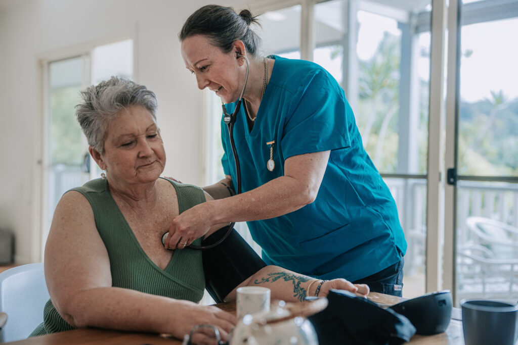 Female Nurse Performing Cardiac Examination On Senior Woman At Dining Table